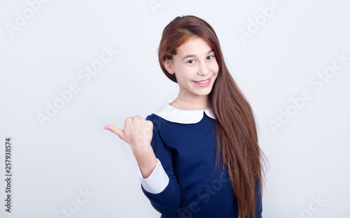 Portrait of a smiling girl pointing her finger to the side on a light background. Schoolgirl.