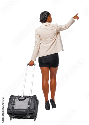 Back view of a black African-American in formal attire walking with a suitcase and pointing hand forward.