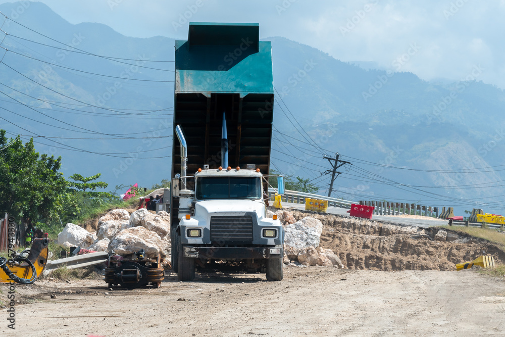 Dumper truck offloading large rock boulders on road construction site