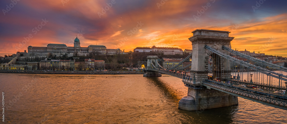Budapest, Hungary - Aerial panoramic view of Szechenyi Chain Bridge with Buda Tunnel and Buda Castle Royal Palace at background with a dramatic colorful sunset - obrazy, fototapety, plakaty 