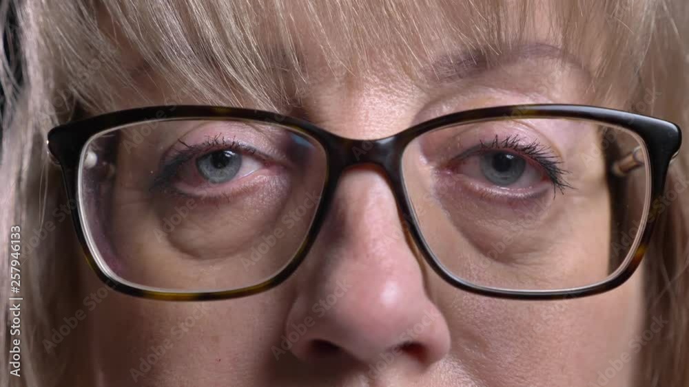Closeup shoot of old caucasian blonde female face in glasses with her eyes looking straight at camera Closeup shoot of old caucasian blonde female face in glasses with her eyes looking straight at camera