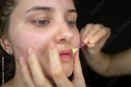 Beautician  makes depilation with hot wax mustache and eyebrow correction on a black isolated background