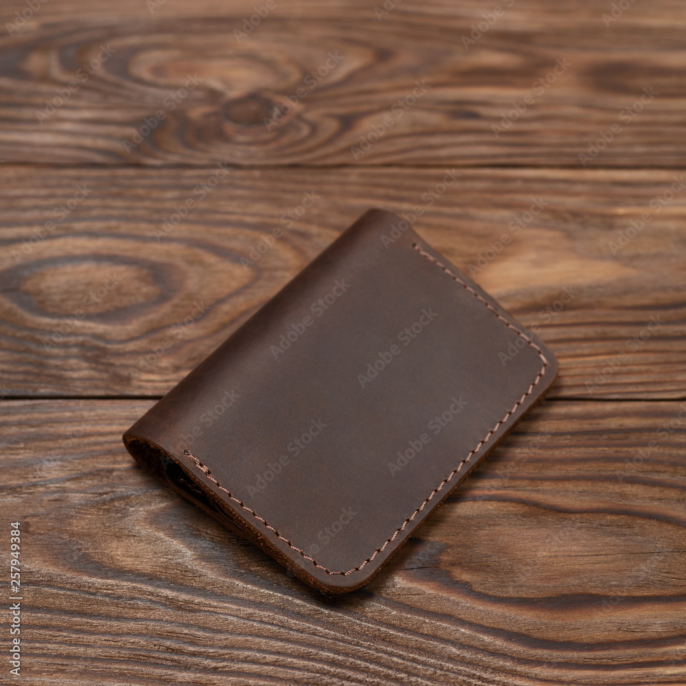Brown two-pocket closed leather handmade cardholder lies on wooden background. Soft focus on background. Stock photo on blurred background. Brown two-pocket closed leather handmade cardholder lies on wooden background. Soft focus on background. Stock photo on blurred background.