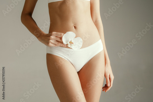 Young woman with epilated bikini zone holding flower isolated on gray studio background. Cut out part of body. Medical problem and solution.