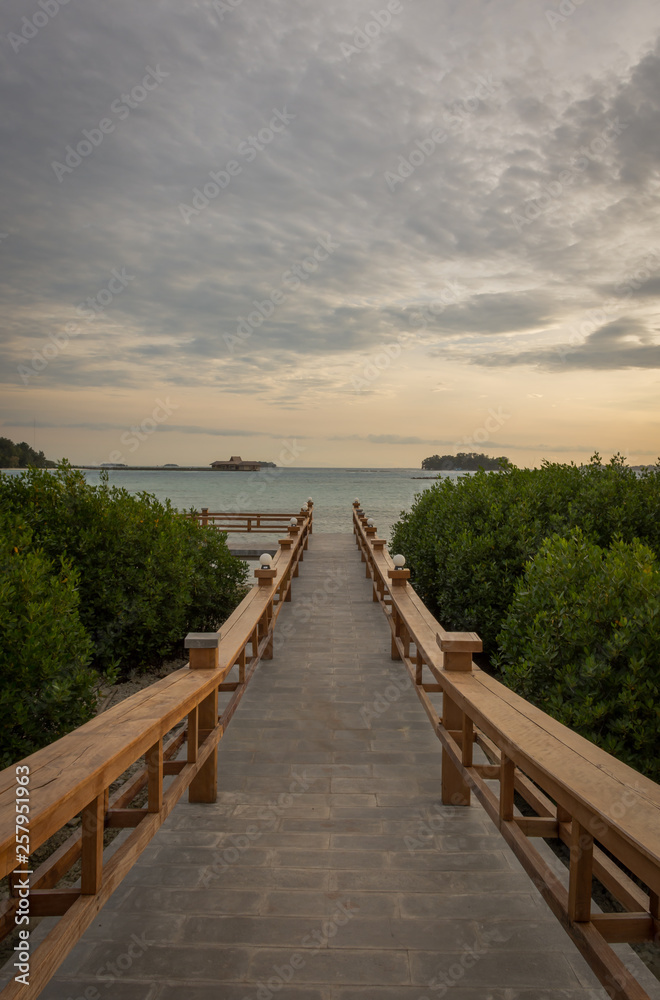 A stone bridge that leads to a place to enjoy the sunset on Royal Island, Indonesia. Surrounded by mangrove forests with beautiful warm skies