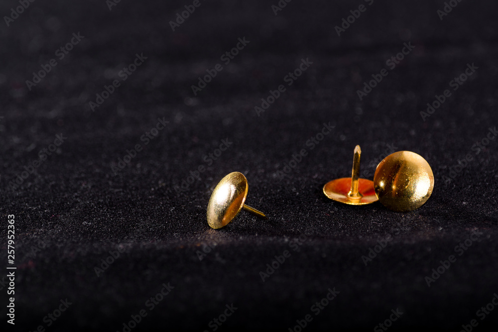 Golden Office pins on a black surface. Stationery. Office tools. Dark photo. Golden Office pins on a black surface. Stationery. Office tools. Dark photo.