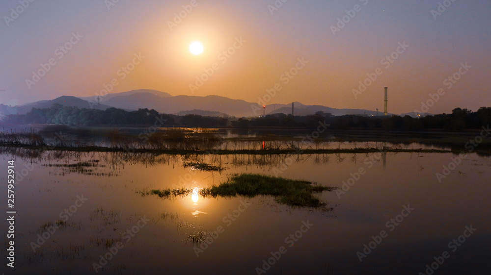 The Full moon rising from behind the hills with the lake in the foreground, Goa, India.