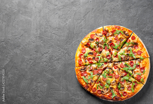 Pizza with Mozzarella cheese, mushrooms, ham, tomato sauce, sausage, pepper, Spices and Fresh arugula. Italian pizza on Dark grey black slate background