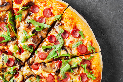 Pizza with Mozzarella cheese, mushrooms, ham, tomato sauce, sausage, pepper, Spices and Fresh arugula. Italian pizza on Dark grey black slate background