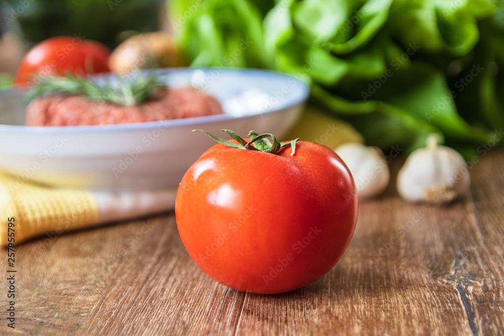 Fresh raw organic tomato on wooden table and other vegetables and minced meat in the background Fresh raw organic tomato on wooden table and other vegetables and minced meat in the background