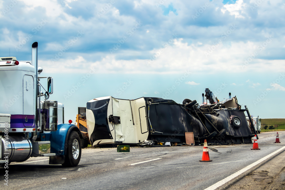 Fifth wheel RV overturned on highway with wench truck trying to get it off the road and two semis parked nearby and traffic cones keeping traffic away Fifth wheel RV overturned on highway with wench truck trying to get it off the road and two semis parked nearby and traffic cones keeping traffic away
