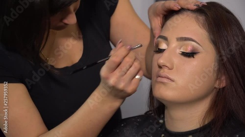 Beauty saloon. Young beautiful girl model is sitting in the chair. Makeup artist makes girl makeup. Brunette in a beauty salon. Makeup artist paints a girl with arrows for the eyes.