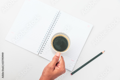 Woman hand holding cup of coffee open notebook Flat lay