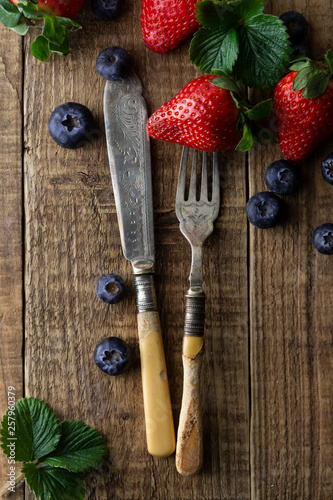 Mixed berries  blueberry  strawberry on wood background with vintage  styled fork and knife. Styled food  fruit background. Template for social media.