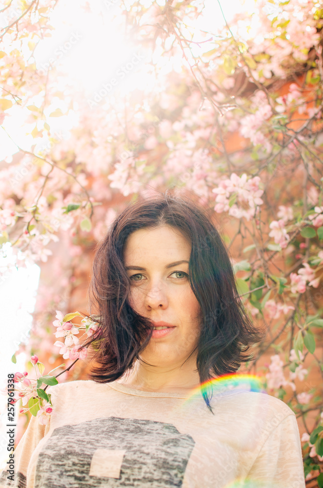Brunette girl stands near a flowering tree. A warm Sunny day, blooming Apple tree. Brunette girl stands near a flowering tree. A warm Sunny day, blooming Apple tree.