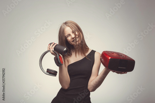 Joyable attractive fashion pretty girl listening music with headphones, speaker, record player, holding thm in hands and wearing red gloves, take pleasure with song. Lifestyle woman concept photo