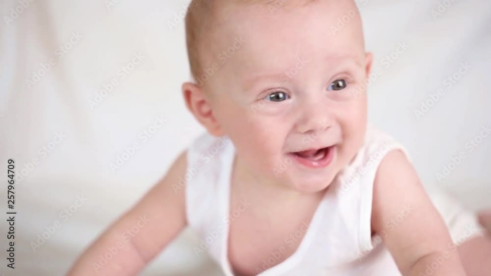 Cute happy 6 month baby boy lying and playing on a white bed Cute happy 6 month baby boy lying and playing on a white bed