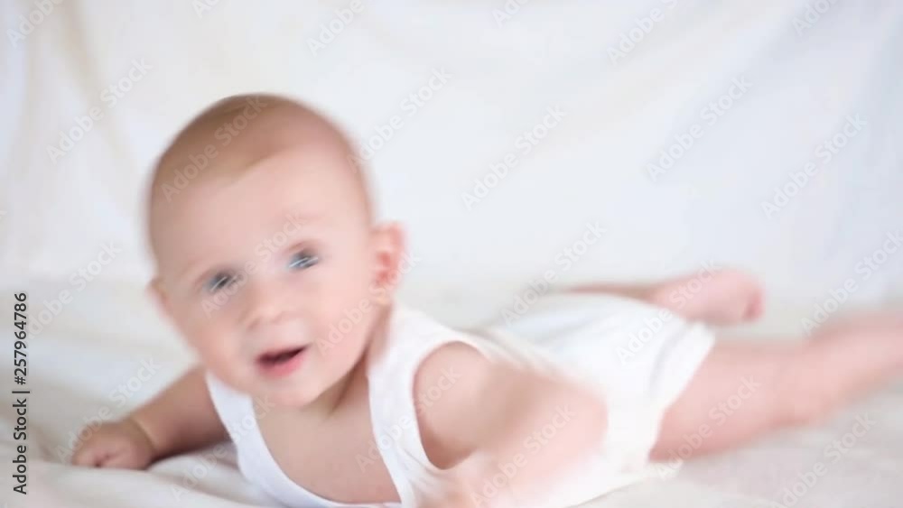 Cute happy 6 month baby boy lying and playing. on a white bed Cute happy 6 month baby boy lying and playing. on a white bed