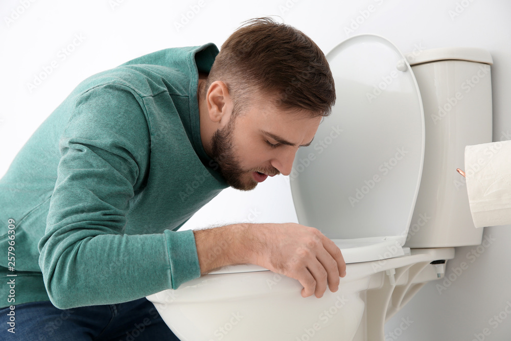 Young man suffering from nausea over toilet bowl indoors Young man suffering from nausea over toilet bowl indoors