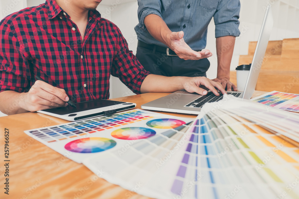 Fototapeta premium Teamwork of young creative designers working on project together and choose color swatch samples for selection coloring on digital graphic tablet at workspace