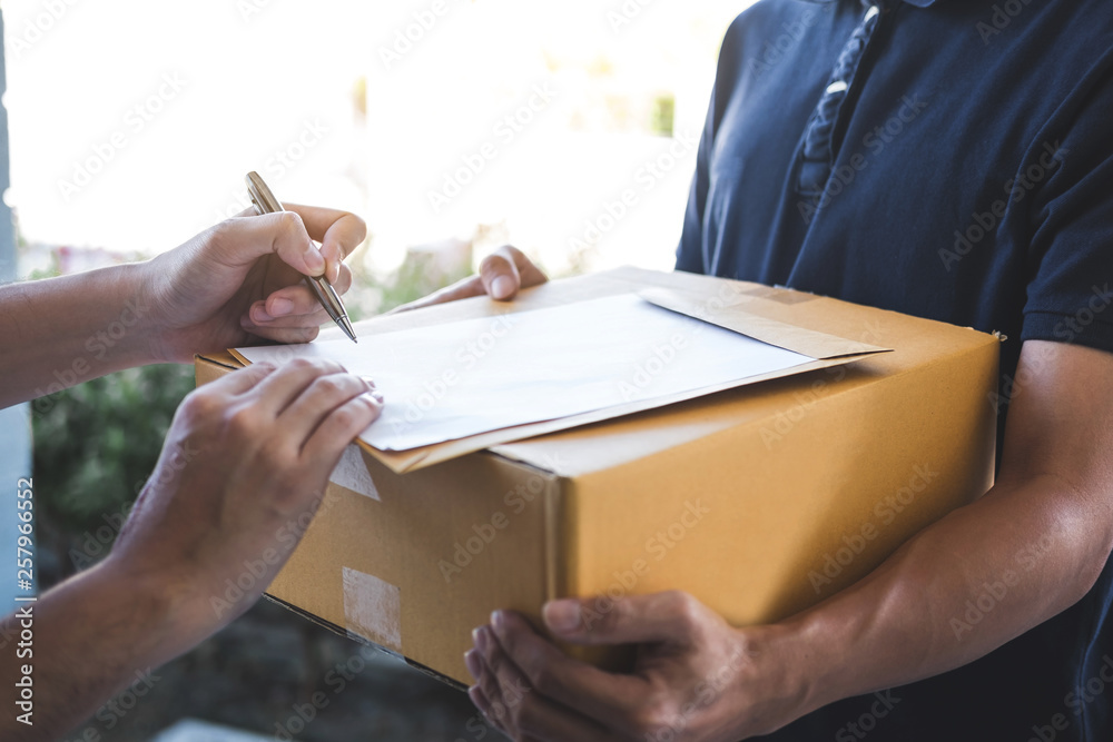 Obraz premium Delivery mail man giving parcel box to recipient and signature form, Young owner signing receipt of delivery package from post shipment courier, Home delivery service and working with service mind