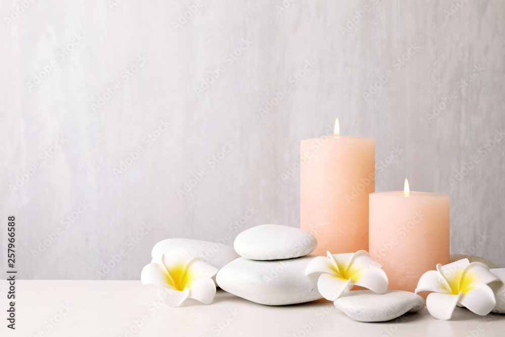 Zen stones, lighted candles and exotic flowers on table against light background. Space for text