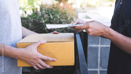 Delivery mail man giving parcel box to recipient and signature form, Young owner signing receipt of delivery package from post shipment courier, Home delivery service and working with service mind