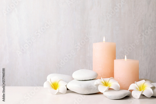 Zen stones, lighted candles and exotic flowers on table against light background. Space for text