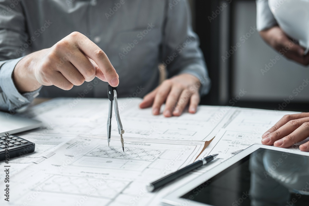 Construction engineering or architect discussing a blueprint and building model while checking information on sketching meeting for architectural project in work site Construction engineering or architect discussing a blueprint and building model while checking information on sketching meeting for architectural project in work site