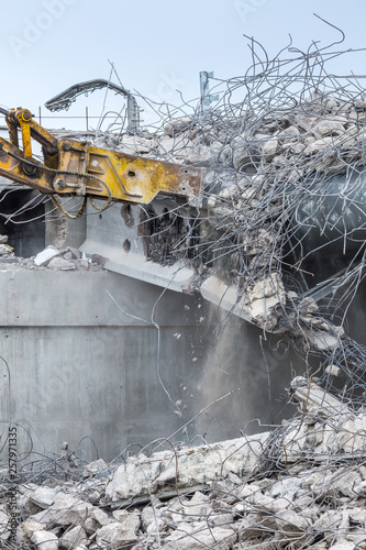 Professional demolition of reinforced concrete structures using industrial hydraulic hammer. Rods of metal fittings. Wreckage and crumbles of concrete.