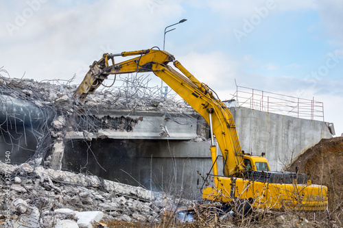 Professional demolition of reinforced concrete structures using industrial hydraulic hammer. Rods of metal fittings. Wreckage and crumbles of concrete.
