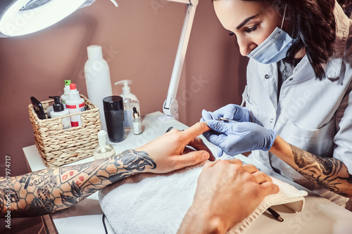 A man receiving a manicure in the beauty salon. Beautician master trimming and removes cuticles. photo