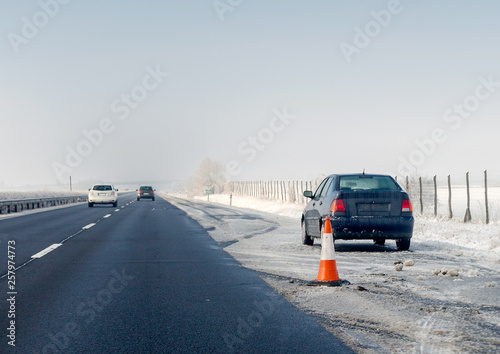 Faulty car and traffic cone on emergency stopping lane on the roadside. Problem with vehicle on winter highway.