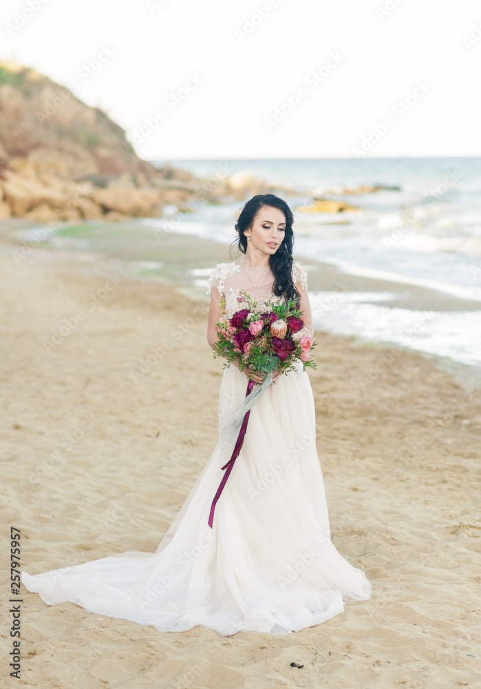 pretty bride in luxury wedding dress with bouquet at the sea side. Wedding by the sea. Bride walking around the sea near the place of the wedding ceremony. pretty bride in luxury wedding dress with bouquet at the sea side. Wedding by the sea. Bride walking around the sea near the place of the wedding ceremony.