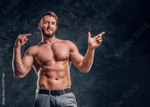 Cheerful shirtless man with the muscular body posing for a camera. Studio photo against dark wall background