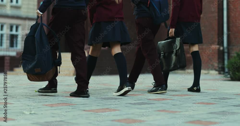 Back view on the feet of the schoolchildren in the uniforms and with bags walkingthe school yard before or after classes. Back view on the feet of the schoolchildren in the uniforms and with bags walkingthe school yard before or after classes.