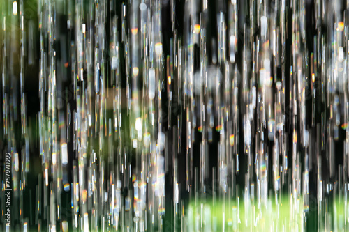 Blurred background pouring water vertically with reflective sun highlights in the garden.