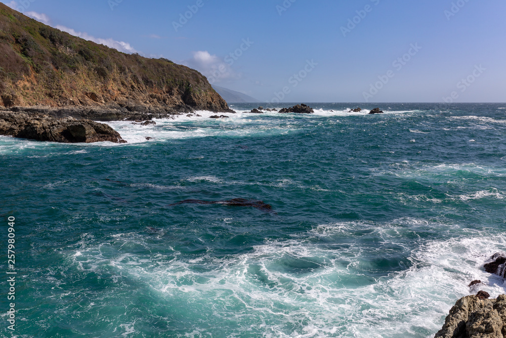 Long exposure of deep blue water, swirling surf, and rocky cliffs of central California
