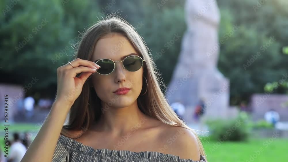 Close-up of pretty young lady taking off glasses smiling looking at the photographer outside in the lovely park. Close-up of pretty young lady taking off glasses smiling looking at the photographer outside in the lovely park.