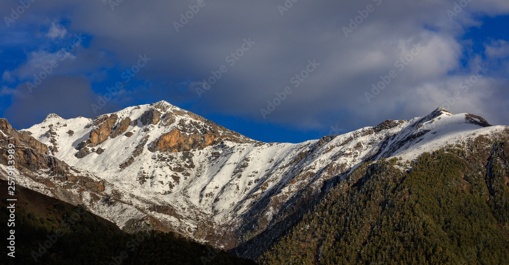 Mountain Landscape, Snow Covered Mountain Range - Daocheng Yading Nature Reserve. Ganzi, Garze, Kham Tibetan area of Sichuan Province China. Dramatic lighting during sunset, Clouds and Blue Sky