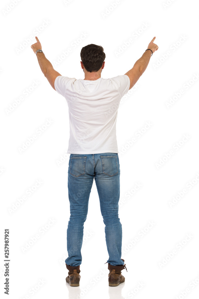 Young Man In Jeans And White T-shirt Is Standing And Showing Something. Rear View Young Man In Jeans And White T-shirt Is Standing And Showing Something. Rear View