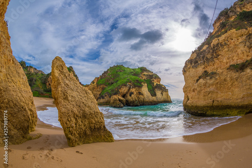 Famous rock formation in a bay on the beach of Tres Irmaos in Alvor, Portimão, Algarve, Portugal, Europe. Praia dos Tres Irmaos.The sun shines through the clouds, the waves roll on the sand