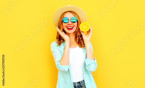 Summer portrait happy smiling woman holding in her hands slices of orange in straw hat on colorful yellow background