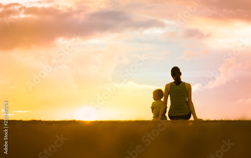 Happy mother and her little boy sitting together watching a beautiful sunset.