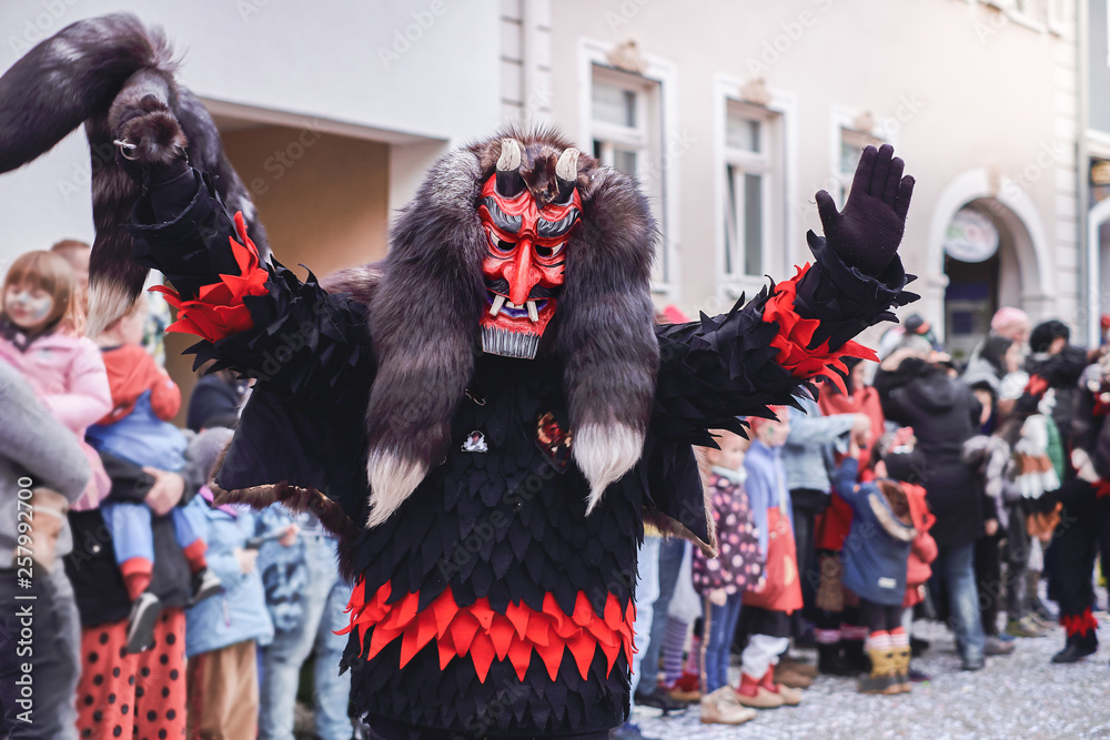 Black devil figure with red mask stretches both arms upwards. Street Carnival in Southern Germany - Black Forest. 