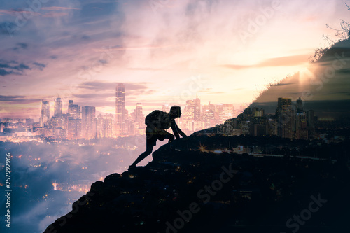 silhouette of man climbing up mountain overlooking city photo