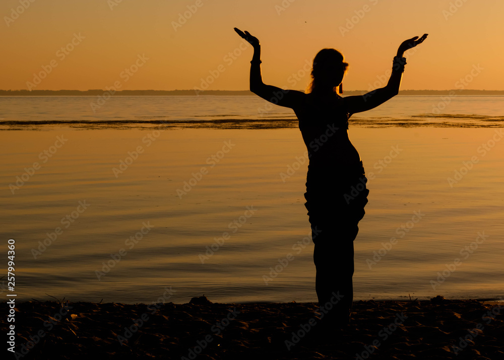 dark silhouette of slim woman dancing tribal dance on beach at dawn