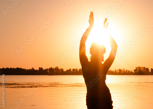 dark silhouette of woman dancing near river coast at dawn