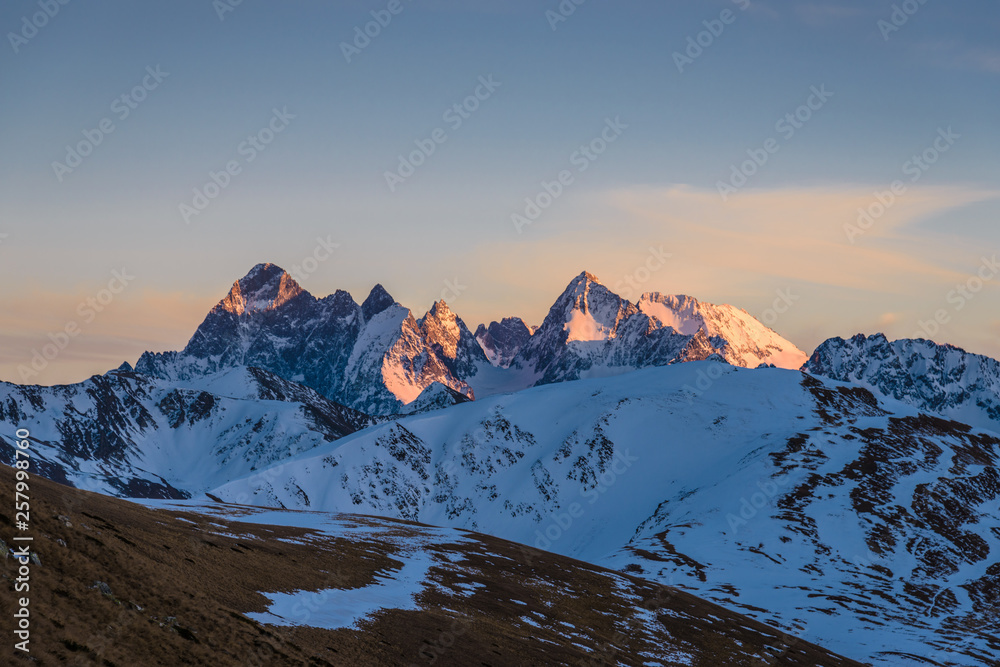 Sunset in the mountains. Snow-capped mountains are illuminated by the orange light of the setting sun
