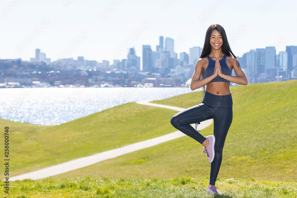 Beautiful woman with long black hair wearing yoga pants and sports bra outside during park workout